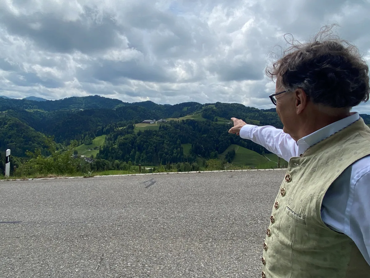 Vom Heimwehbänkli in Sternenberg kann man den Weiler Unterer Wolfsberg gut sehen. Roberto Fröhlich steht an der Strasse und zeigt auf den Weiler auf der gegenüberliegenden Talseite.